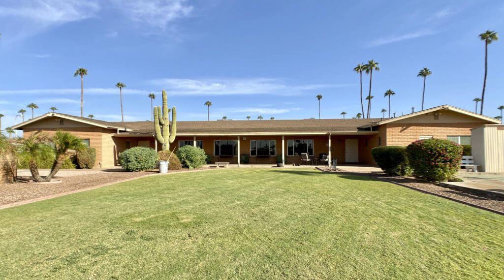 One-story brick building with a large front lawn area composed of grass, cacti, and other desert plants near Apache Junction, Arizona.