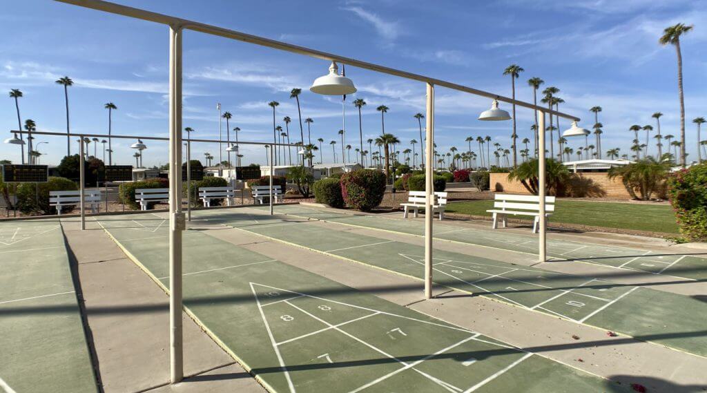 Outdoor shuffleboard courts with pole lamps and metal benches next to them